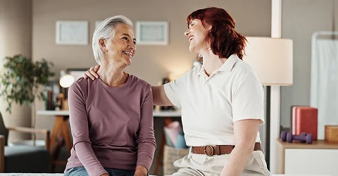 Two women sitting on a couch smiling and talking in a cozy living room.