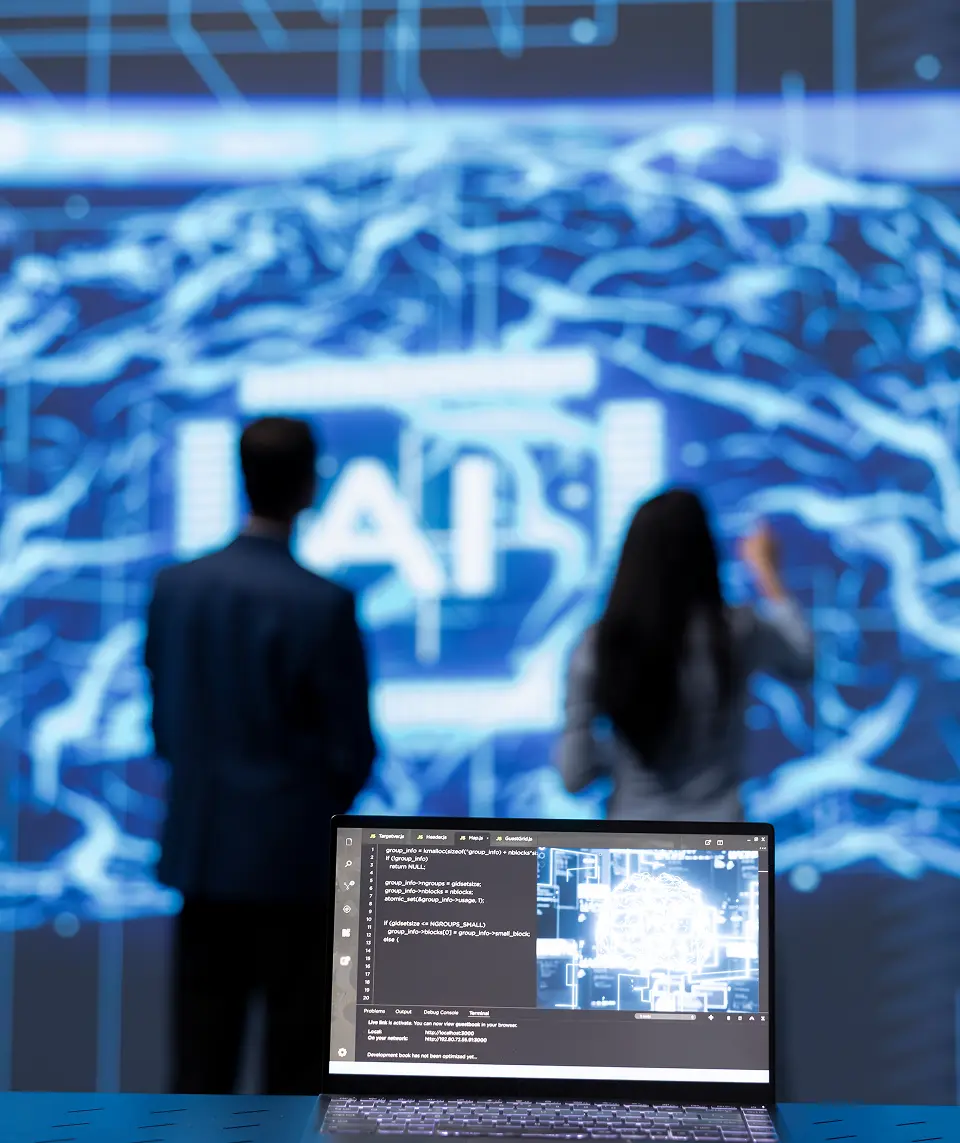 Laptop displaying code in the foreground with two professionals analyzing a large digital brain interface in the background, suggesting AI or data science work.