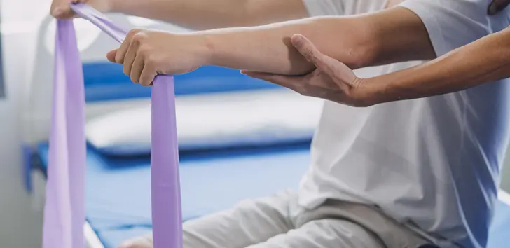Physical therapist guiding a patient's arm during a resistance band exercise in a clinical setting