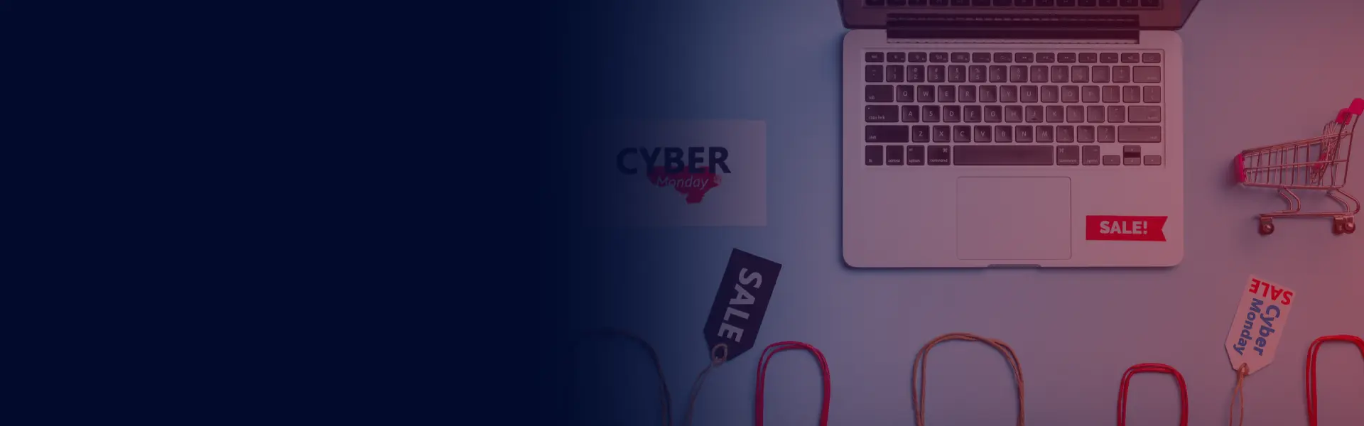 Laptop, shopping bags, sale tags, and a mini shopping cart with Cyber Monday branding on a flat lay surface