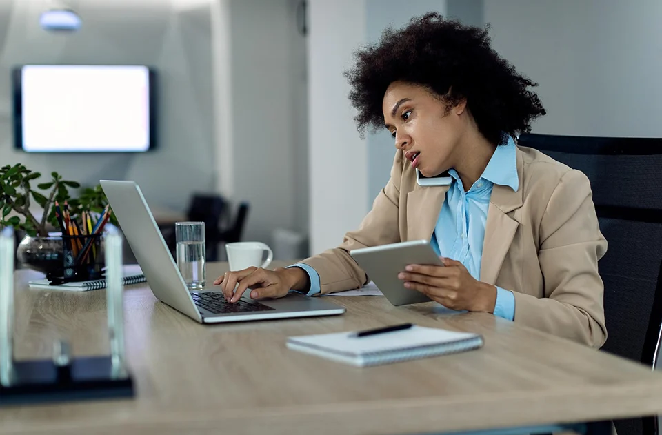 Businesswoman using a laptop and tablet while talking on the phone